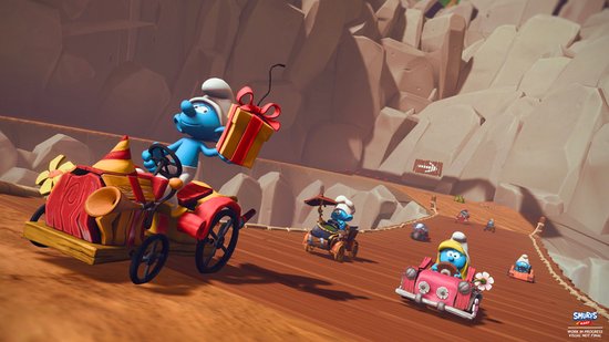 Smurf in rode en gele kart met cadeaubox, rijdend op een helling. Roze kart rechts.