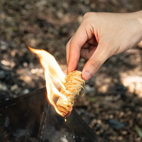 Hand houdt een brandende aanmaakwokkels boven een barbecue.