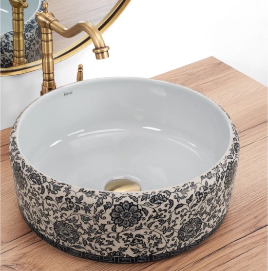 Lavabo blanc à motif floral bleu et blanc et robinet en laiton sur meuble en bois.