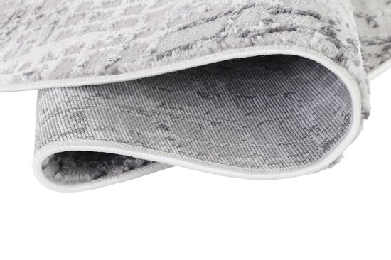 Detail van de onderkant van een rond grijs vloerkleed met een geruit patroon en witte bies.