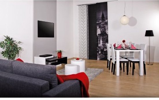 Moderne woonkamer met grijze bank, tv aan de muur en witte eettafel.