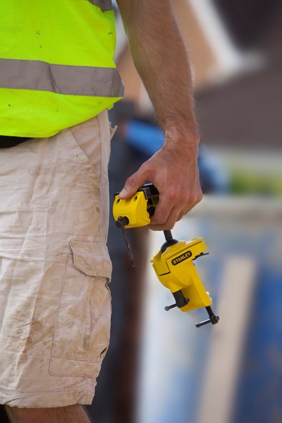 Gele multifunctionele boorklem van Stanley in de hand van een man met een werkbroek.