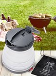 Opvouwbare waterkoker in een buiten setting bij een barbecue, met een picknickmand en drankjes.