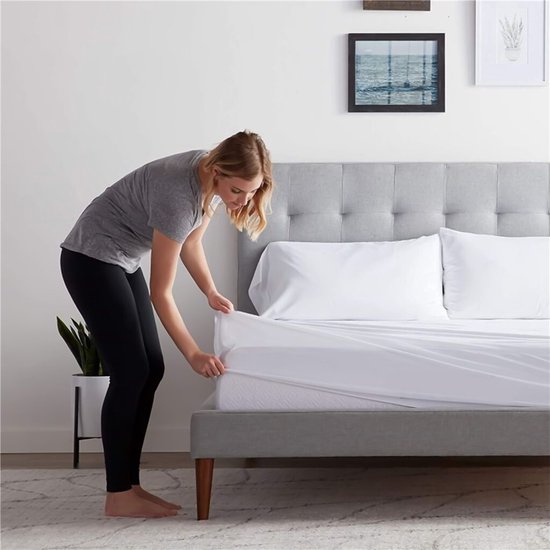 Een vrouw legt een wit hoeslaken op een bed.