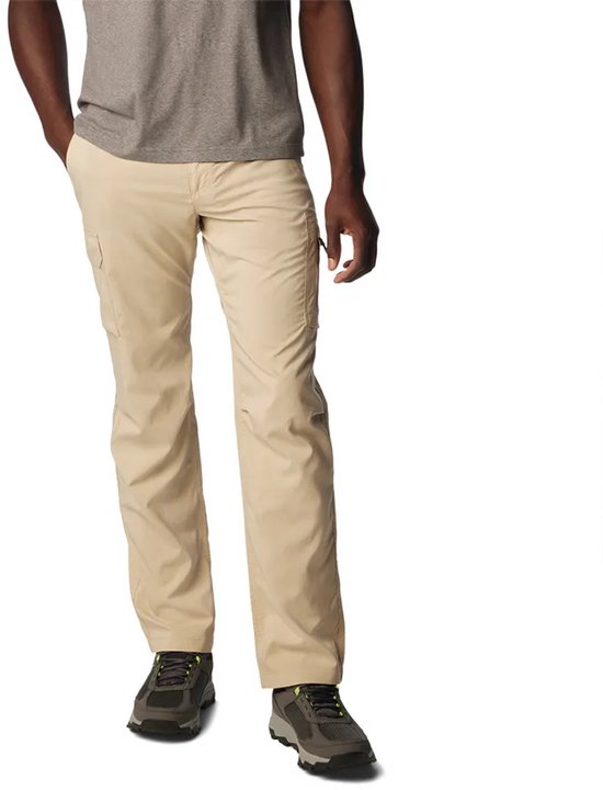 Een man met een grijze T-shirt en beige cargo broek met cargo zakken, staande met zijn handen in de zakken.