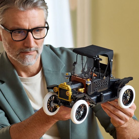 Man houdt een zwarte LEGO Ford Model T met witte banden vast. Zwarte kap, gouden koplampen.