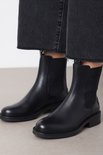 Dichtbij van zwarte leren Chelsea boots gedragen bij grijze jeans met rafels.
