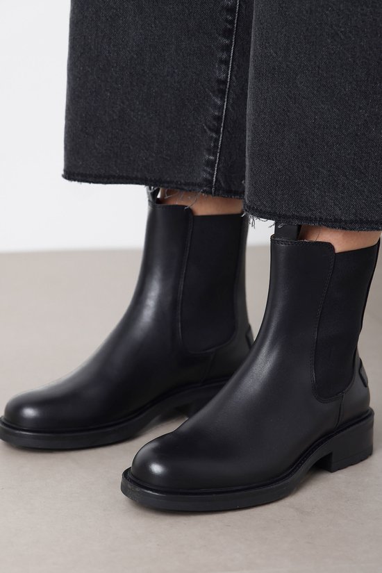 Dichtbij van zwarte leren Chelsea boots gedragen bij grijze jeans met rafels.