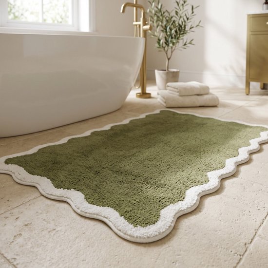 Groene badmat met witte, geschulpte rand naast een wit bad en gouden kraan.
