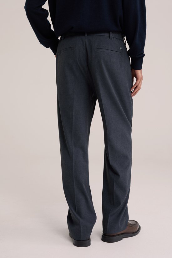 Man in donkerblauwe trui en donkerblauwe pantalon met bandplooi, van achteren gezien.