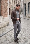 Man met bruin vest, grijs geruit overhemd en grijze chino, kijkend naar een ticket.