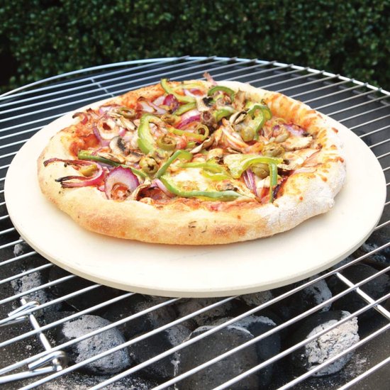 Een gebakken pizza met paprika, ui, champignons en olijven op een beige pizzasteen boven een barbecue.