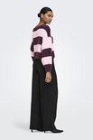 Een model draagt een trui met horizontale strepen in roze en bordeauxrood, met een zwarte broek.