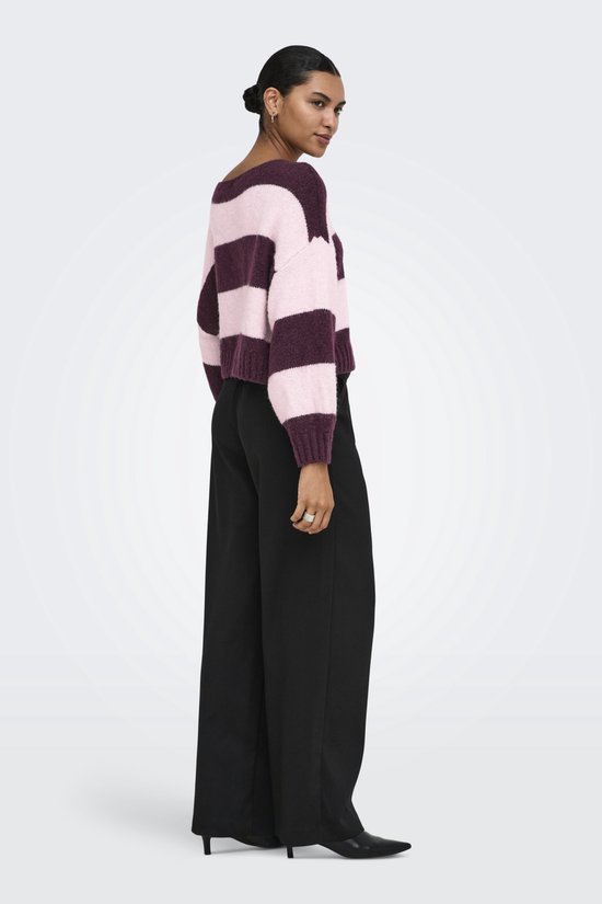 Een model draagt een trui met horizontale strepen in roze en bordeauxrood, met een zwarte broek.