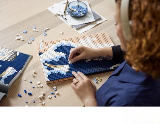 Une femme construit avec des briques LEGO une version 3D de La Grande Vague, avec des briques bleues et blanches pour les vagues.