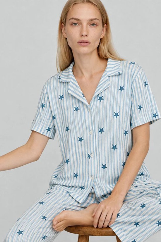 Model in pyjamaset met sterrenprint en lichtblauwe strepen, zittend op een houten kruk.