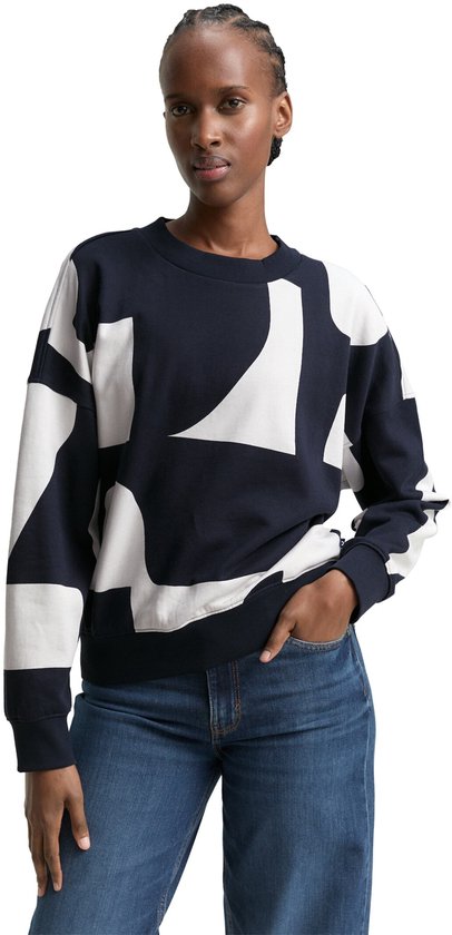 Model in een donkerblauwe sweater met oversized witte abstracte print. Jeans en de sweater met lange mouwen zijn gecombineerd.