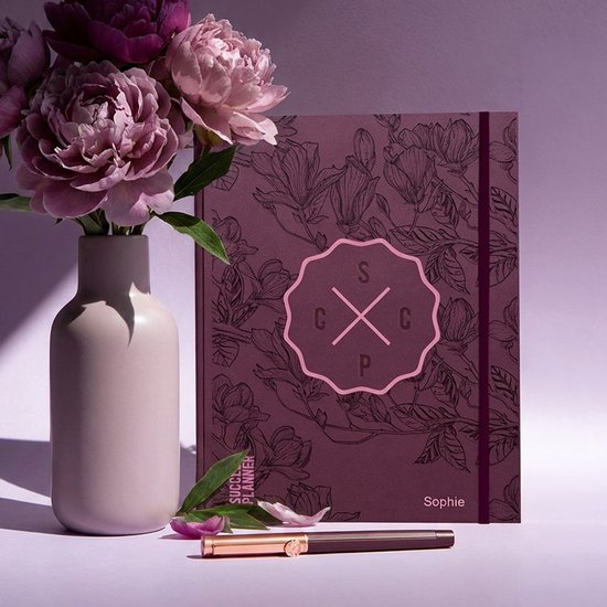 Paarse planner met bloemenprint naast een vaas met bloemen en een pen.