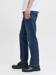 Zijaanzicht van een man met tatoeages in een witte T-shirt en een donkerblauwe jeans.
