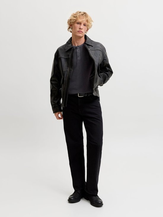 Model draagt een antracietgrijze henley met lange mouwen onder een zwarte leren jas en zwarte jeans.