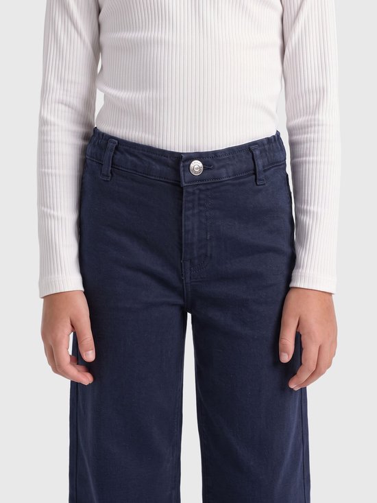 Voorkant van een marineblauwe jeans met wijde pijpen, met een knoopsluiting en riemlussen, gedragen met een witte top.
