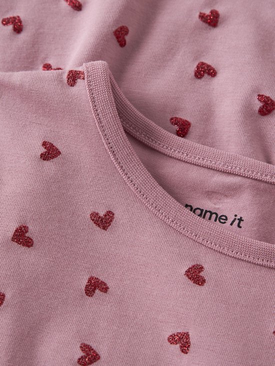 Close-up van de halslijn van een lichtroze jurk met rode glitter hartjes.