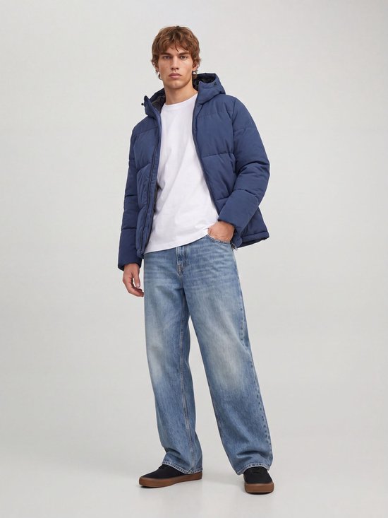 Man draagt een blauwe pufferjas met capuchon, wit T-shirt en wijde jeans.