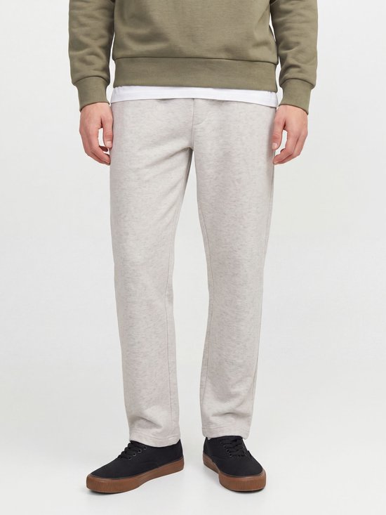 Model draagt een lichtgrijze joggingbroek, een olijfgroene trui en zwarte sneakers.