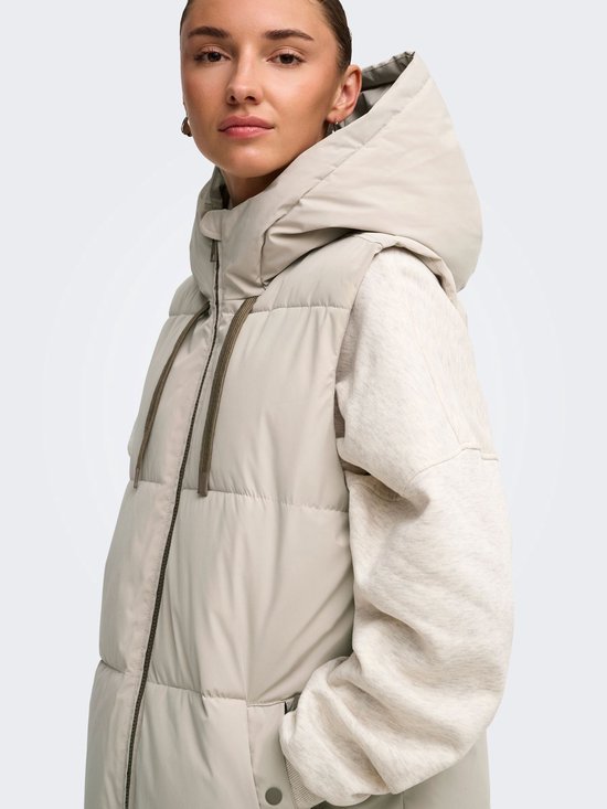 Close-up van het gezicht van een model die een lange beige bodywarmer met capuchon draagt.