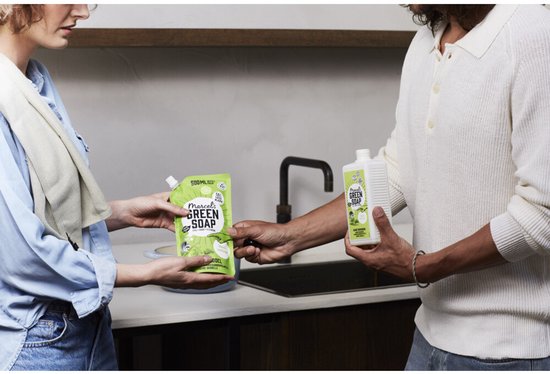 Vrouw en man in keuken; zij neemt groene Marcel's Green Soap navulzak aan van de man die een lege fles vasthoudt.