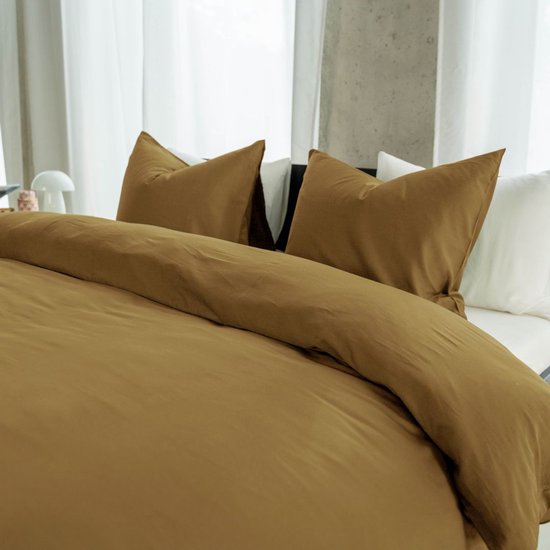 Bed met bronzen dekbedovertrek en kussenslopen, deels bedekt met witte lakens.