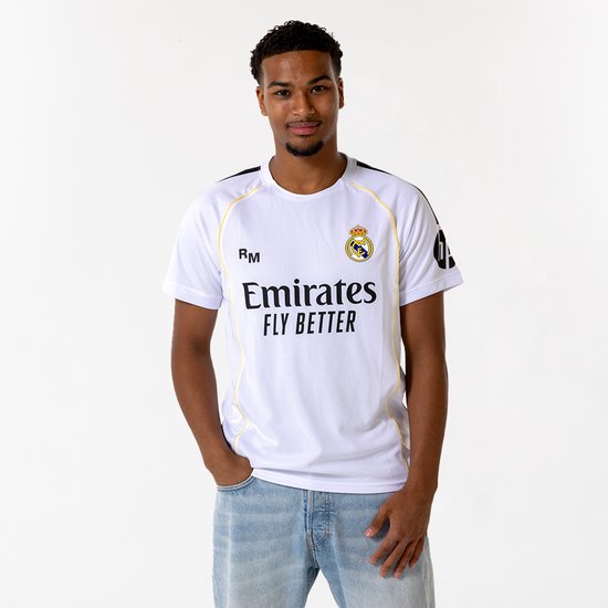 Jonge man draagt een wit Real Madrid voetbalshirt met 'Emirates FLY BETTER' opdruk en spijkerbroek.