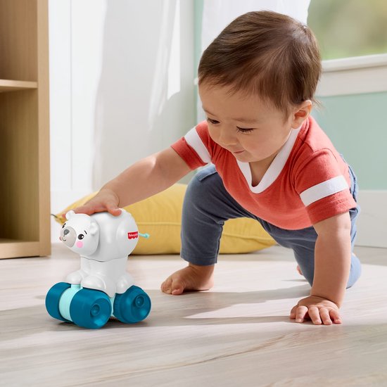 Baby met oranje shirt kruipt naar een witte Fisher-Price beer op blauwe wielen.