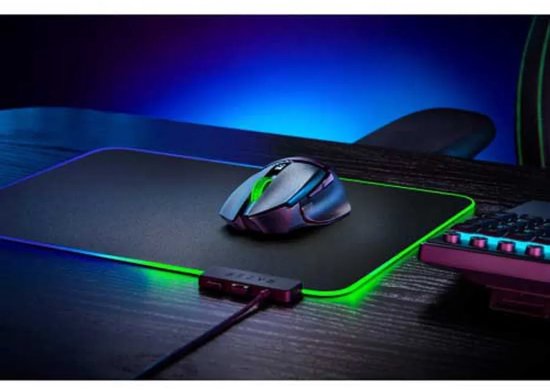 Zwarte Razer gaming muis met groene details, staand op een zwart gamingmuismat met gloeiende groene en blauwe randen, naast een toetsenbord.