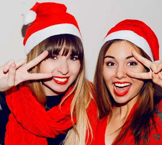 Twee jonge vrouwen met kerstmutsen en sjaals, lachend en zwaaiend met vrede-tekens.