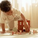 Kind speelt met houten brandweerkazerne, brandweerwagen en poppetjes.