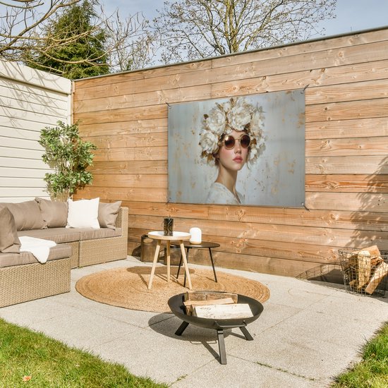 Meisje met zonnebril en grote witte bloemenkrans op een rustige, gouden achtergrond, hangend aan een houten schutting.