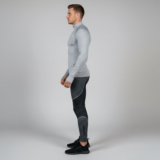 Man in profiel met grijze top en zwarte legging met grijze lijnen en ruitpatroon. Zwarte sneakers.