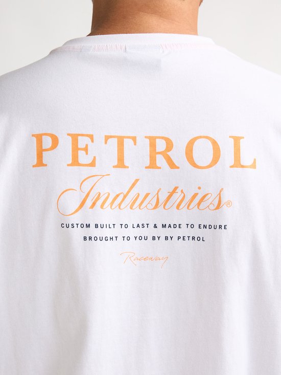Detail van de rug van een wit T-shirt met grote oranje opdruk: PETROL Industries, CUSTOM BUILT TO LAST & MADE TO ENDURE, BROUGHT TO YOU BY BY PETROL, Raceway.