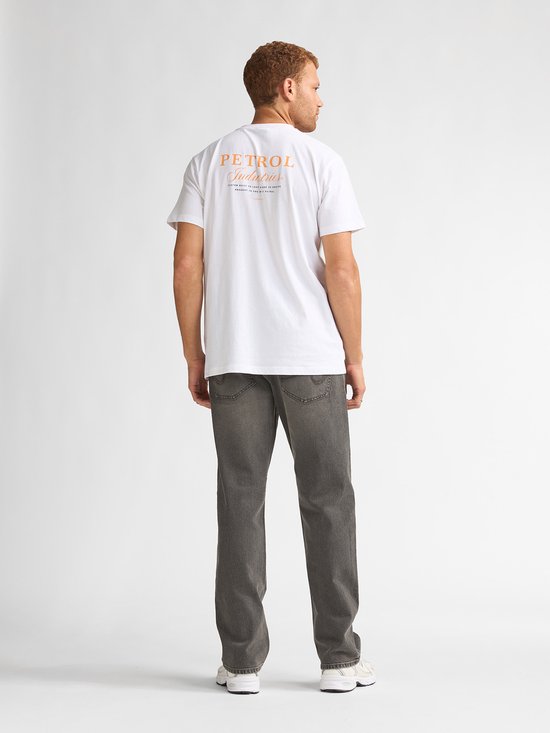 Man met rood haar, gekleed in een wit T-shirt met oranje rugopdruk en grijze jeans, van achteren gezien.