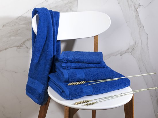 Serviettes bleu classique sur une chaise blanche avec des tiges de blé et un fond en marbre.