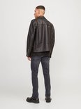 Man in zwarte bikerjack en grijze jeans, gezien vanaf de achterkant.
