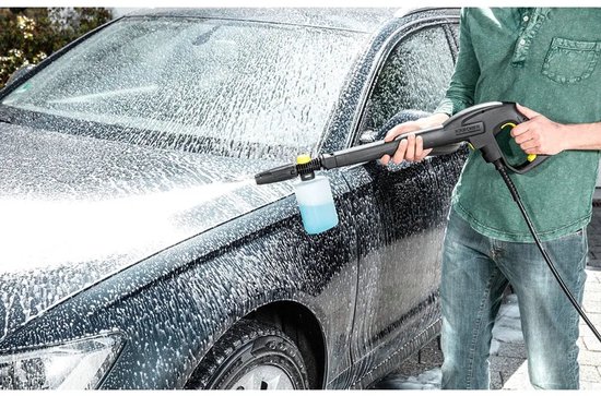 Man gebruikt schuimspuit op auto, met blauwe vloeistof in reservoir.