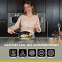 Een vrouw met een beige trui bakt eieren in een koekenpan met een houten spatel. De tekst "Geschikt voor alle warmtebronnen" staat onderaan.