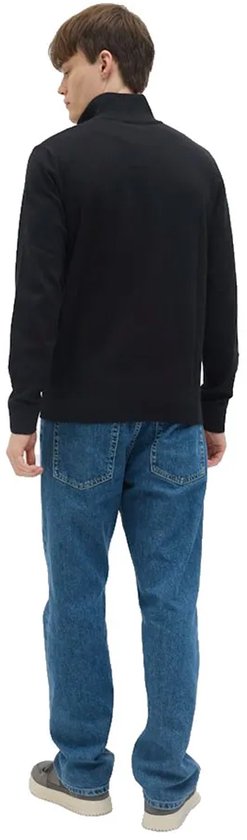 Man in zwarte trui met hoge hals en halve rits, gedragen met jeans.