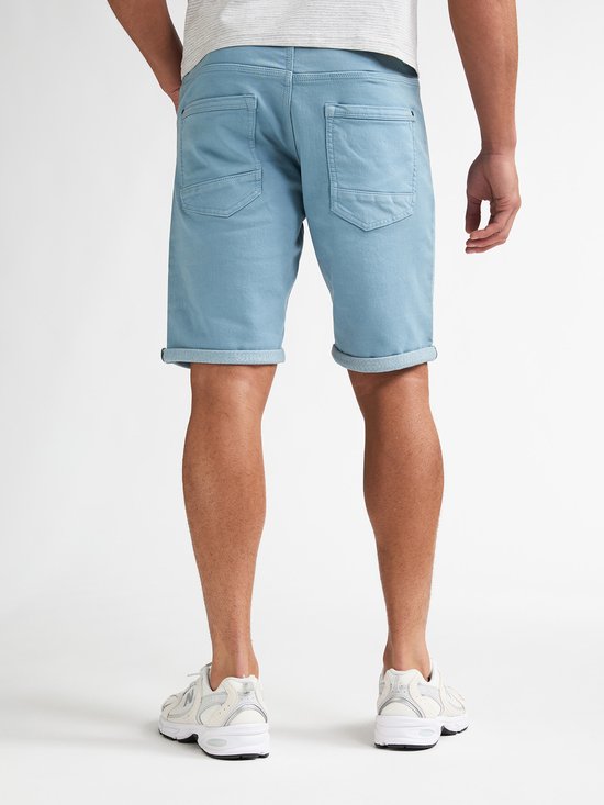 Achterkant van een man in een lichtblauwe denim short met opgerolde zoom en witte sneakers. Slim fit model.