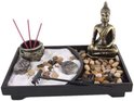 Zen tuin met Boeddhabeeld, wierookhouders met rode wierookstokjes, stenen en een harkje.