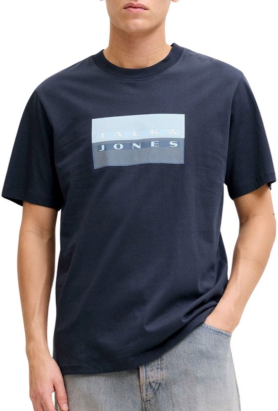 Man met donkerblauw T-shirt met 'JACK & JONES' print en grijze jeans, hand in broekzak.