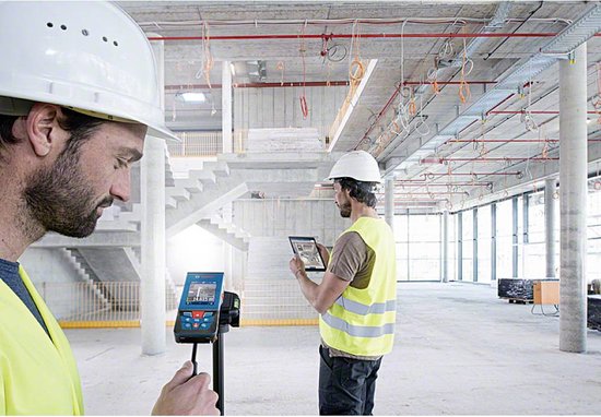 Twee bouwvakkers met helmen en hesjes in een gebouw, één met een Bosch laser afstandsmeter.