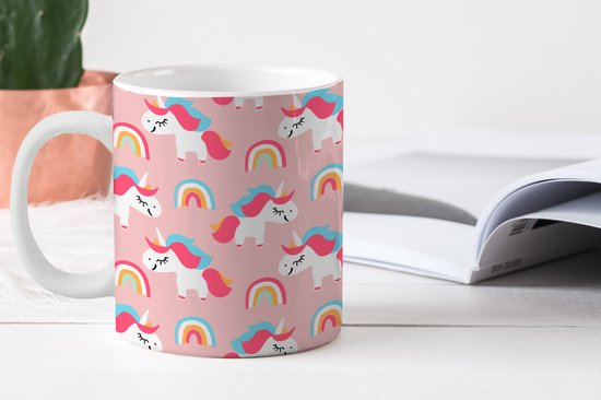 Witte mok met een roze patroon van eenhoorns en regenboogjes, naast een open boek.
